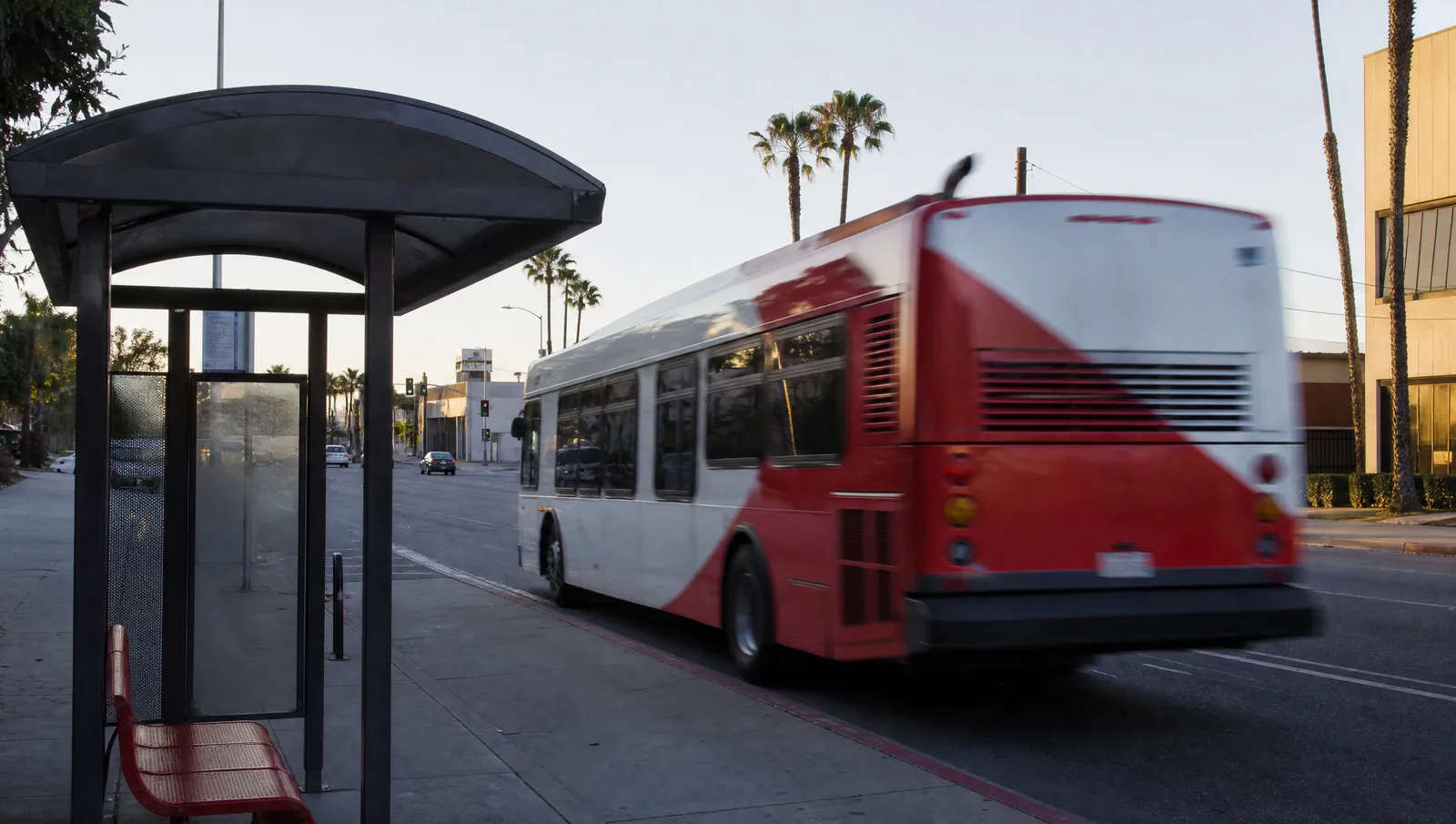 A city transit bus pulling away from a curbside bus stop on a wide Los Angeles boulevard