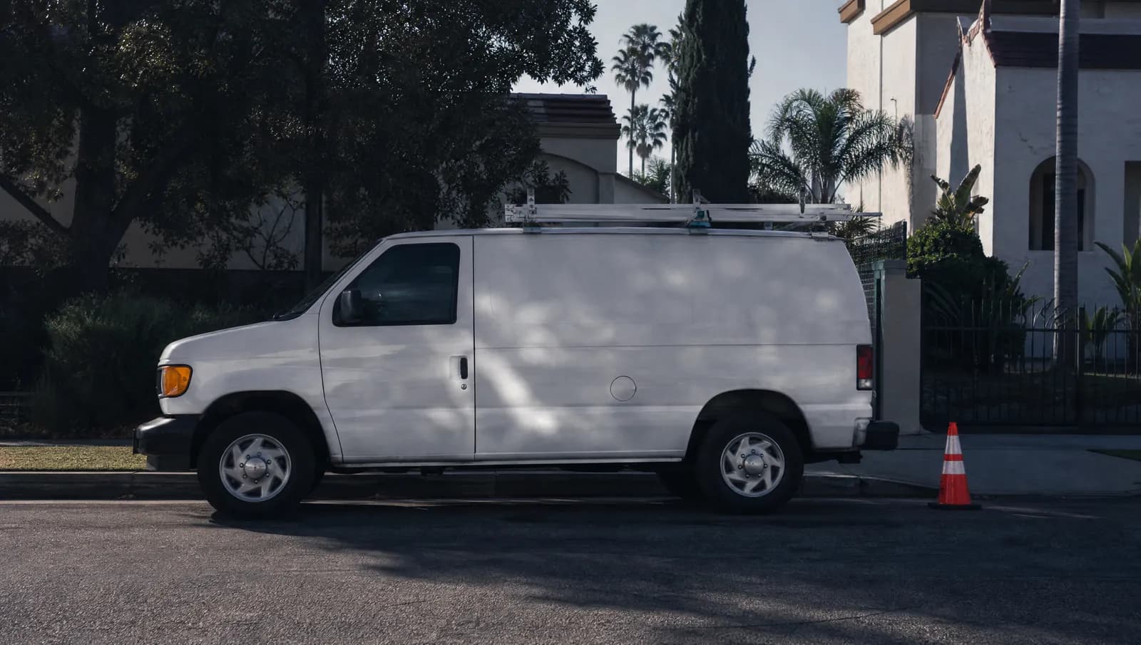 A white work van with a ladder rack parked at a curb on a Los Angeles residential street