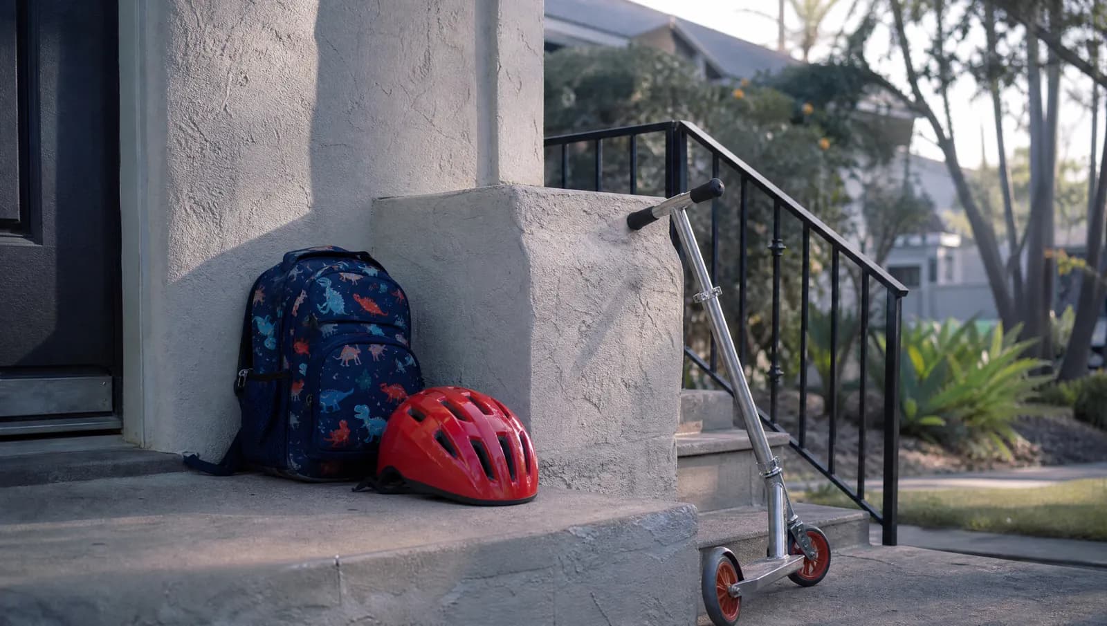 A child's red bicycle helmet and a small backpack on the front step of a house