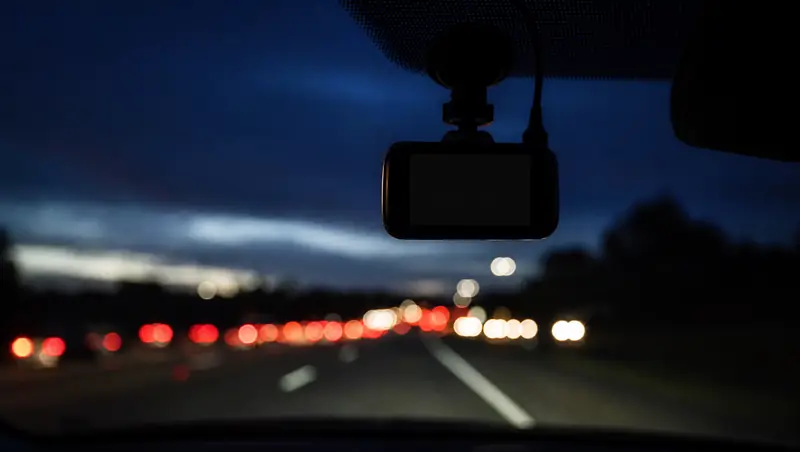 A dashcam mounted on a windshield with freeway headlights blurred ahead at dusk.