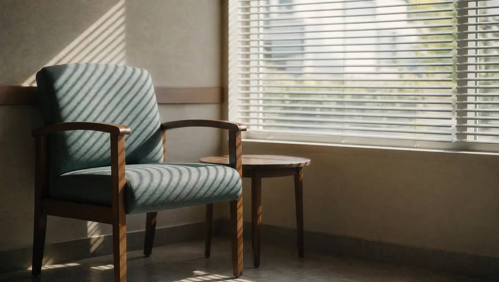 An empty waiting-room chair beside a clinic window with morning light falling through the blinds.