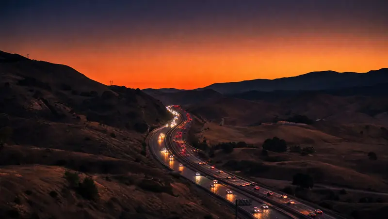 Headlights wind up the 101 freeway through the Conejo Grade hills at sunset.