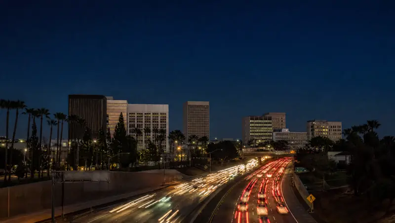 Traffic streams along the 5 freeway below the Santa Ana civic center towers at dusk.